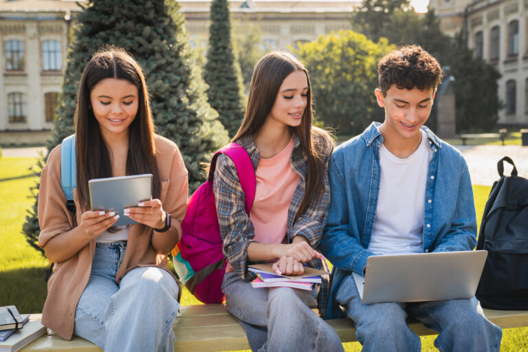 Group of students using gadgets and talking near campus