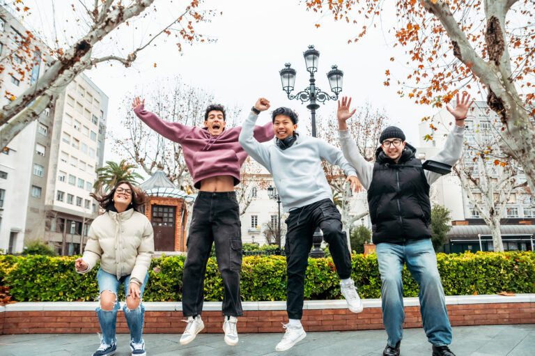 Multi-ethnic college friends leaping playfully, sharing exuberant moment in urban green space, radiating youthful camaraderie and multicultural connection